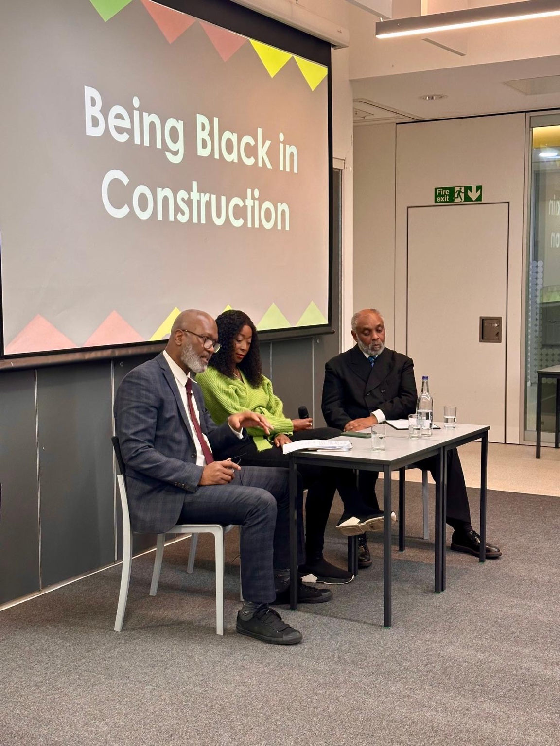 Three panellists at the Being Black in Construction event, with the event title on the screen